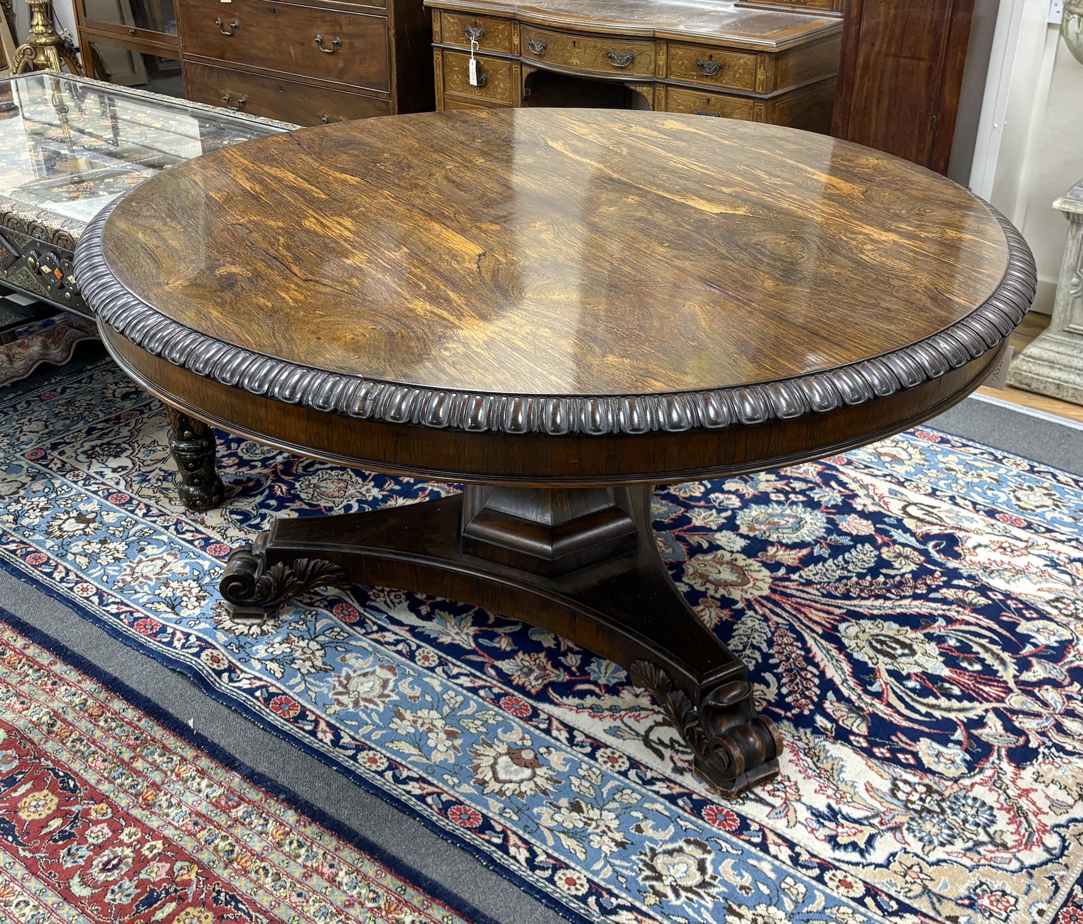 A William IV circular rosewood centre table, the tilt top with lappet carved edge on single tapered hexagonal column, tripartite slab base with scrolled feet, diameter 135cm, height 72cm